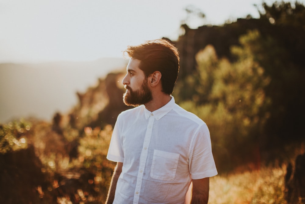 man in white collard shirt standing surround by trees under white sky