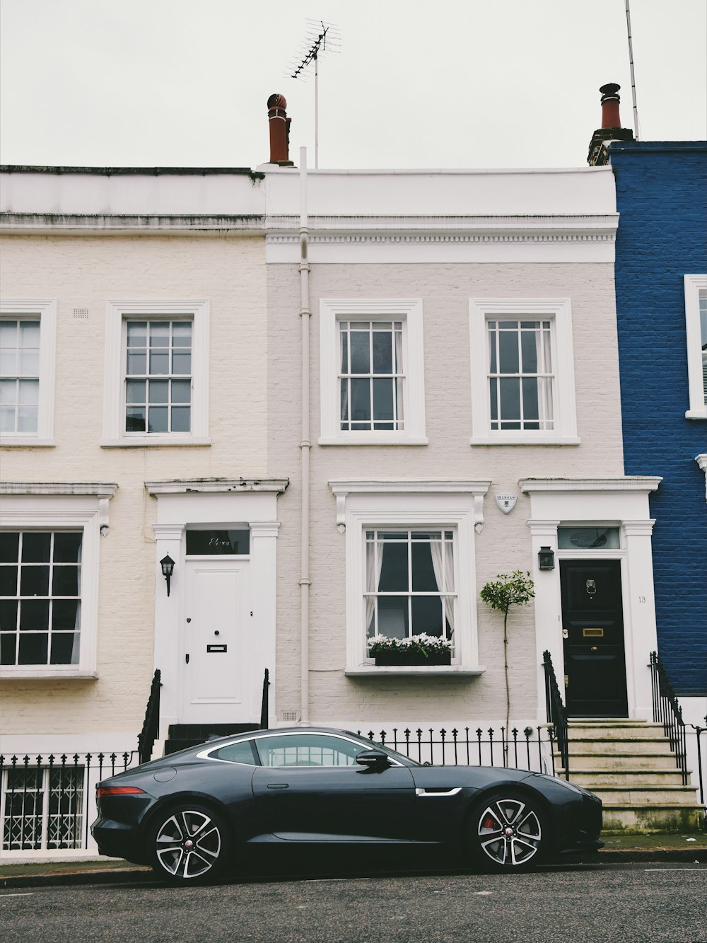 gray coupe parked beside white concrete multi-story house during daytime