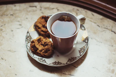 A variety of crunchy cookies stacked neatly beside a steaming cup of tea