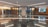 A modern indoor space with polished dark marble floors, bright linear ceiling lights, and wooden paneling along the walls. The area features glass doors with signage for 'The Wash' and a digital display on the wall showing multiple data screens.