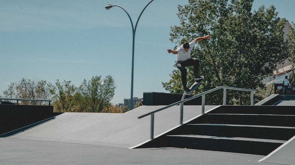 man in white shirt performing skateboard stunts on rail during daytime