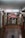 A red car is suspended on a vehicle lift in the middle of an auto repair garage. The garage has a high ceiling, fluorescent lights, and appears to be equipped with various tools and machinery along the walls. The floor of the garage is slightly wet and has a drain in the middle. There is a sign in Italian visible on the right side of the image.