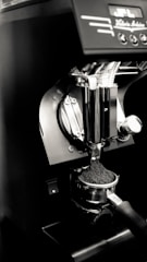 An espresso machine's portafilter is being filled with freshly ground coffee. The setup is sleek and modern, featuring a metallic finish with some controls visible at the top.