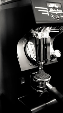 An espresso machine's portafilter is being filled with freshly ground coffee. The setup is sleek and modern, featuring a metallic finish with some controls visible at the top.