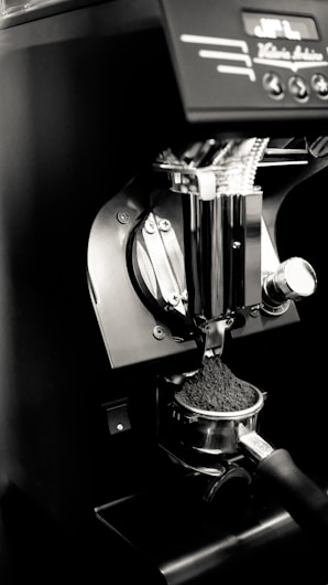 An espresso machine's portafilter is being filled with freshly ground coffee. The setup is sleek and modern, featuring a metallic finish with some controls visible at the top.