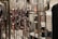 The image features a close-up view of a metallic, reflective, geometric structure with square shapes. In the background, there are blurred images of clothing items, including a black garment and other patterned clothing.