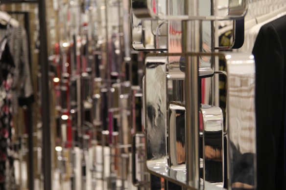 The image features a close-up view of a metallic, reflective, geometric structure with square shapes. In the background, there are blurred images of clothing items, including a black garment and other patterned clothing.