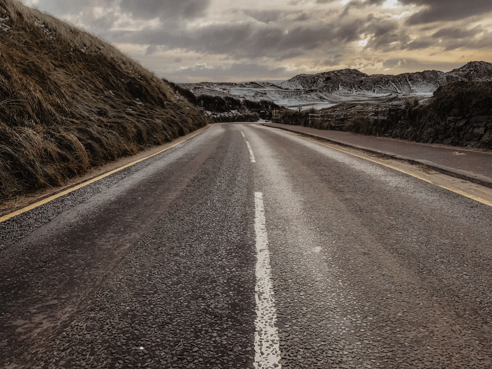 empty concrete road by mountain under gray skies