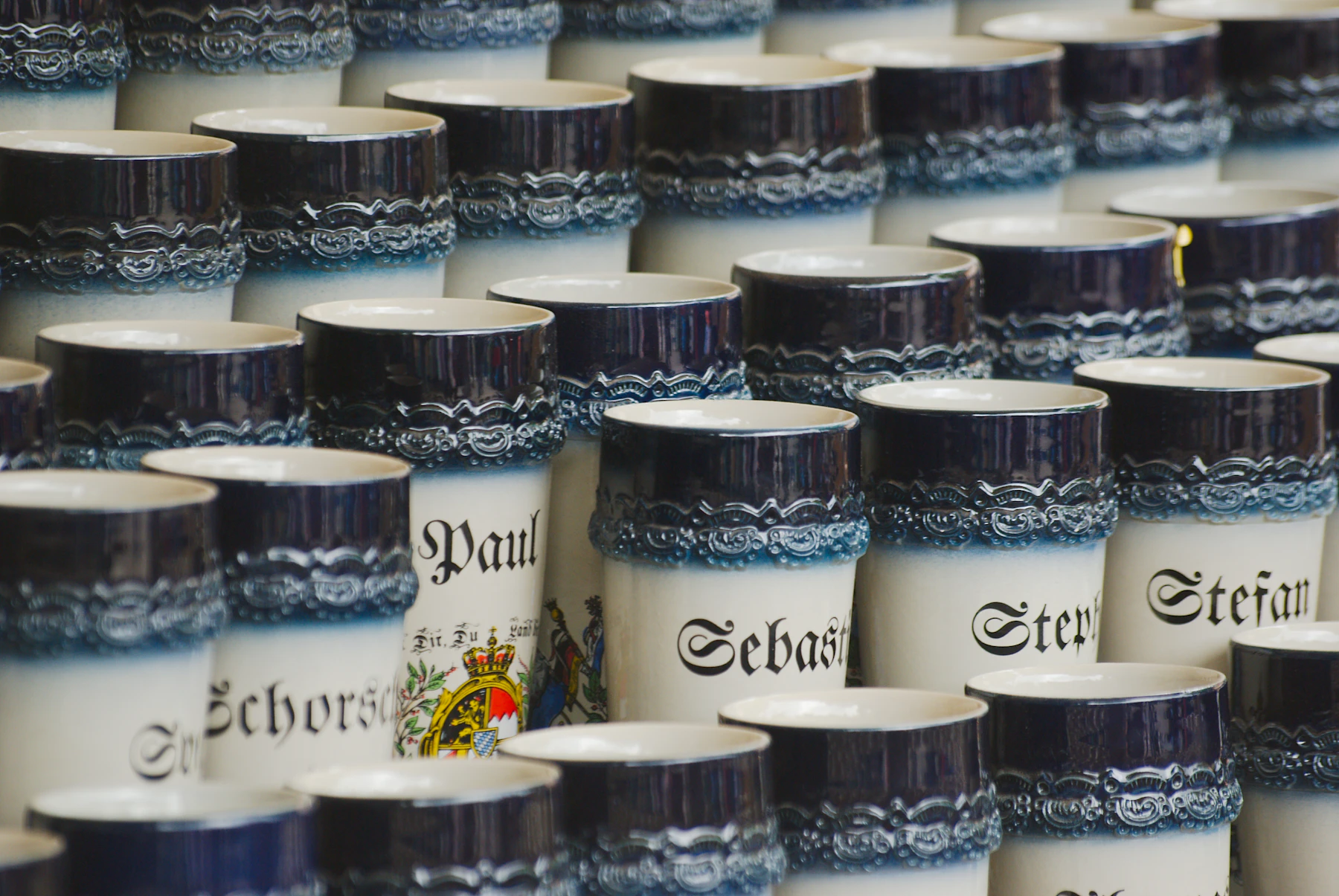 Rows of souvenir stoneware mugs with cobalt blue bands and first names painted on the front