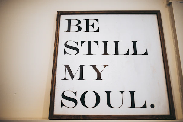 A close-up of a soft cotton shirt featuring the verse 'Be Still and Know' in elegant script with a subtle cross background.