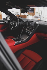 A sleek and modern car interior featuring luxurious red and black leather upholstery. The dashboard is equipped with a high-tech display and control panel. The steering wheel has an emblem, and the overall design conveys elegance and sophistication.