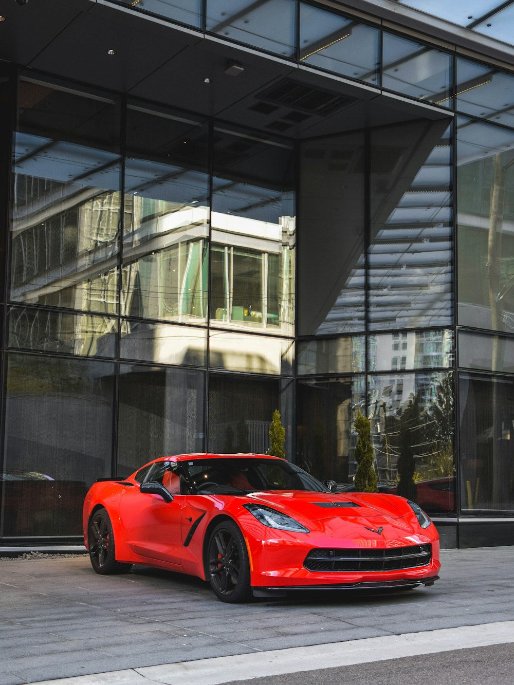 cupê esportivo Corvette vermelho ao lado do prédio de vidro durante o dia