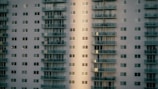 A high-rise residential building with a modern design featuring multiple floors and numerous windows. The structure is characterized by protruding balconies aligned in stacks, providing an urban and geometric aesthetic.