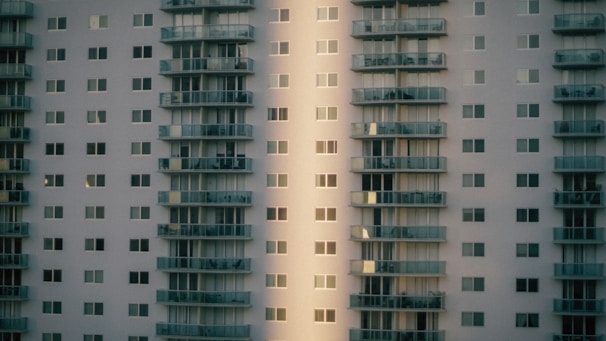 A high-rise residential building with a modern design featuring multiple floors and numerous windows. The structure is characterized by protruding balconies aligned in stacks, providing an urban and geometric aesthetic.
