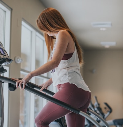 woman wearing white tank top exercising on gym equipment