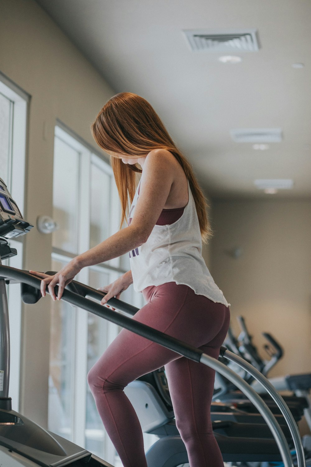 woman wearing white tank top exercising on gym equipment