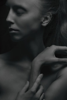 A grayscale image of a serene person with closed eyes. The person's head is slightly tilted, and the hands are elegantly positioned near the face, conveying a sense of peace.