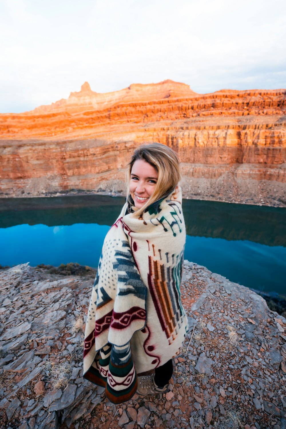 smiling woman standing on rock beside body of water