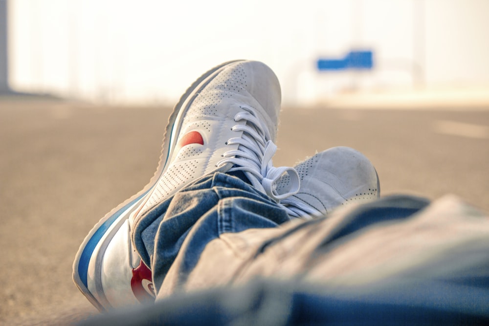 person in white-and-red Nike low-top sneakers and blue denim pants sitting on road during daytime