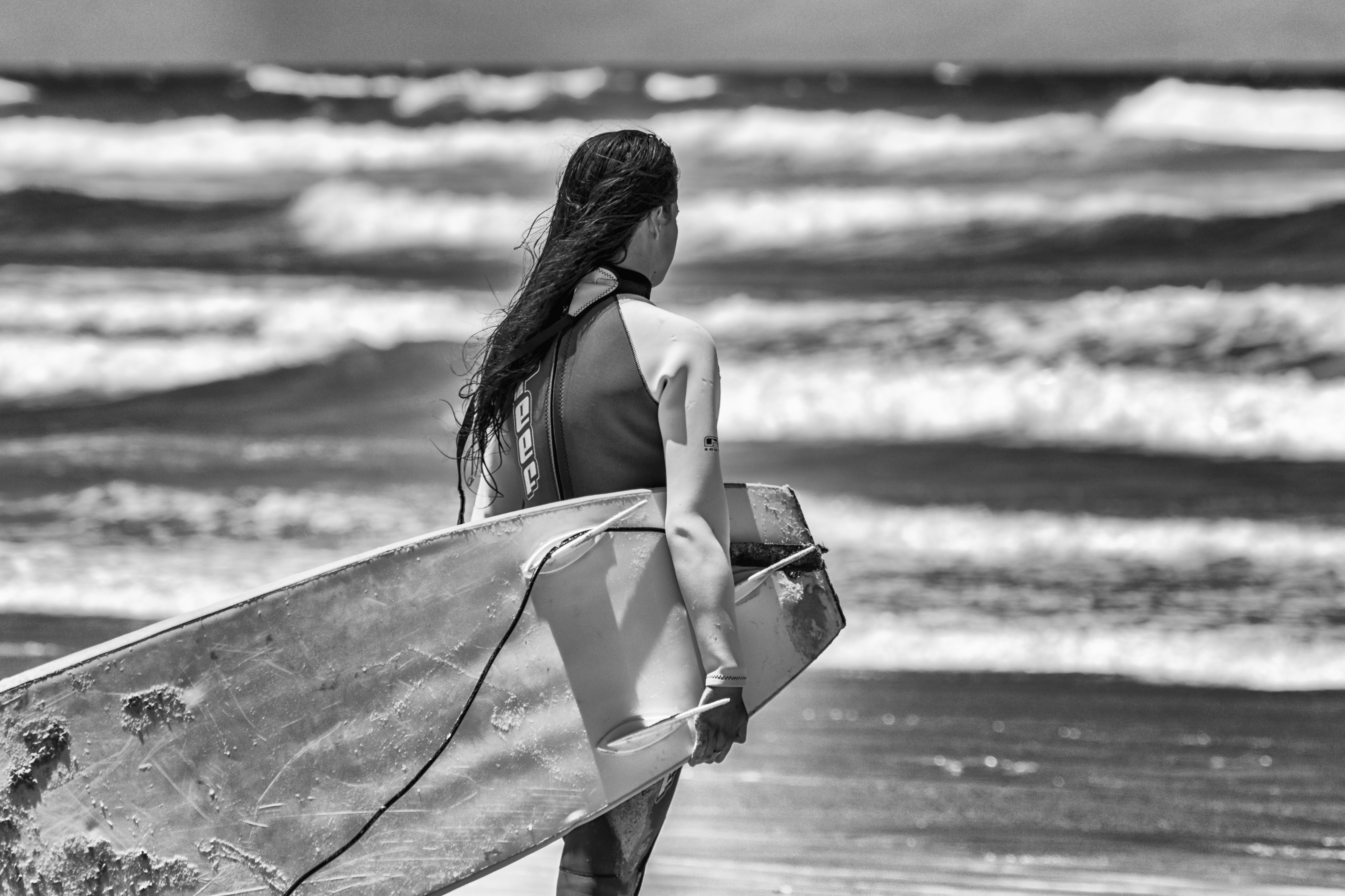 海に面しながらサーフボードを運ぶウェット スーツの女性の写真 Unsplashで見つけるグレーの無料写真