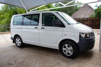 White Toyota Hiace van with tinted windows, parked in front of a modern office building.