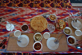 A beautifully arranged table with vibrant Middle Eastern, Chinese, and North African dishes on traditional Saudi mats and dalla pots.