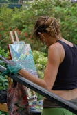 An artist's hands painting on a canvas outdoors.