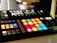 A music production controller with an array of brightly lit, colorful pads arranged in a grid. These pads are surrounded by various buttons and knobs for controlling music software. The background is slightly blurred, highlighting the focus on the controller.