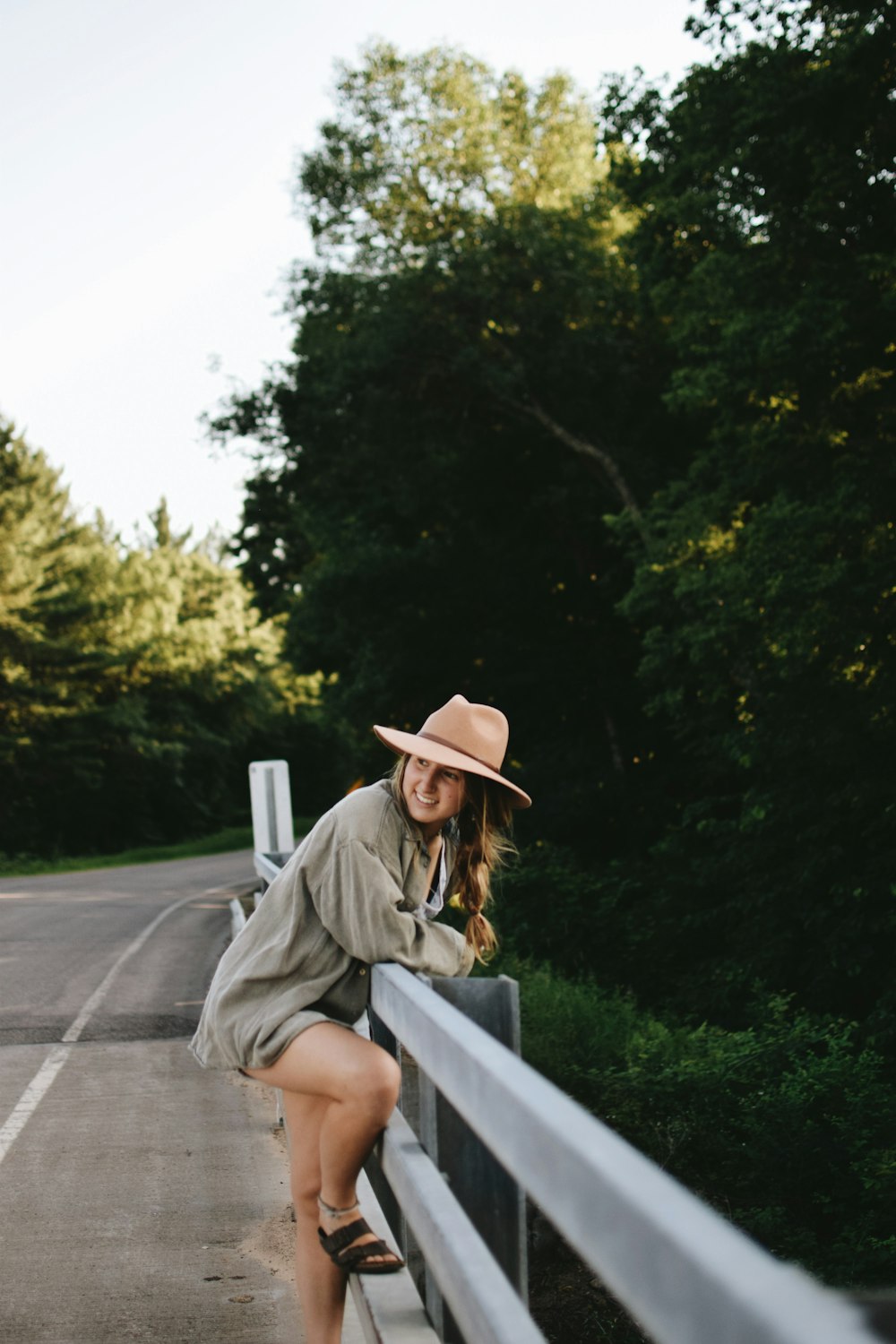 woman standing at road beside green trees during daytime