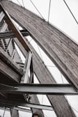 An architectural structure featuring large, wooden arches supported by metal beams and cables. The image includes a mesh netting detail and part of a person's head at the bottom.
