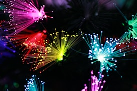 Vibrant and colorful fibers of light radiate in various directions, creating an intricate display. The fibers are primarily pink, red, yellow, and blue, their tips glowing brightly against a dark background, producing a mesmerizing and abstract visual effect.