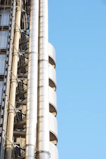 A skilled plumber installing pipes on a modern high-rise construction site under a clear sky.