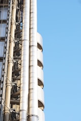 A section of a modern building featuring exposed steel pipes and structural elements against a clear blue sky.
