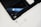 On a clean surface, there is a sleek black smartphone with a reflective Apple logo, a pair of white wireless earbuds, a matching white charging case, and a stylus pen. The setup is organized and minimalist, creating a tech-focused aesthetic.