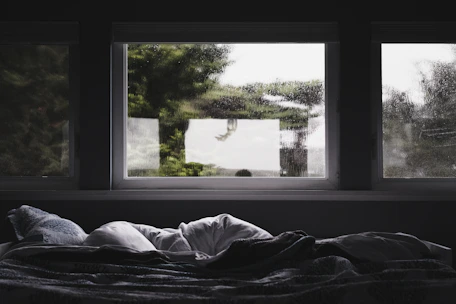 A cozy bed with soft blankets and a window view of autumn trees.