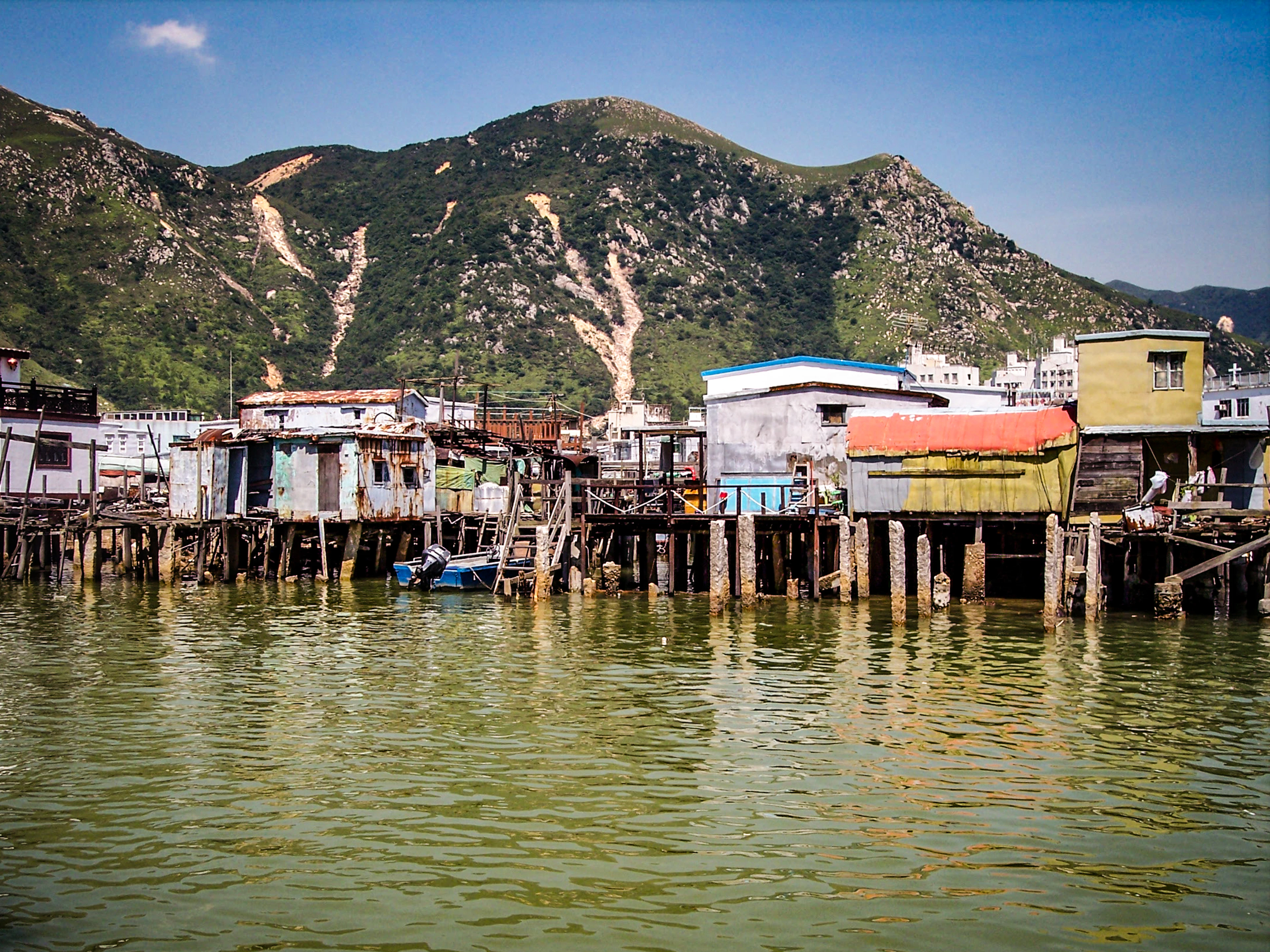 Namai ant polių prie vandens Tai O žvejų kaimelyje, už jų – žalios Lantau kalvos