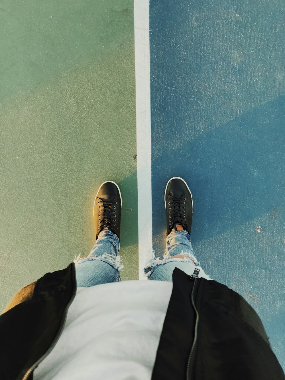 person wearing blue denim jeans standing on blue and gray concrete pavement