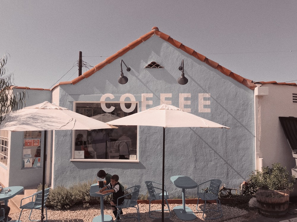 due ragazzi al tavolo da pranzo all'aperto in metallo blu vicino alla caffetteria blu durante il giorno