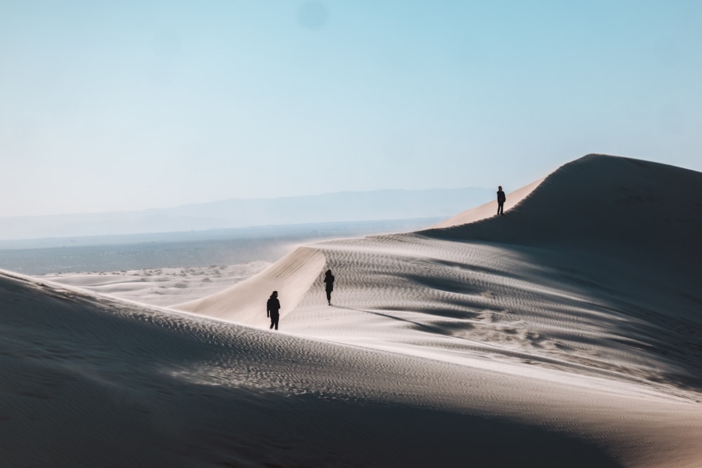 silhouette of three people standing on desert sand during daytime