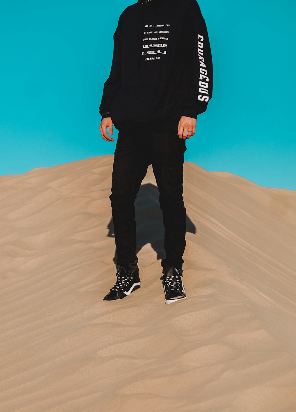 man in black jacket and black pants standing on brown sand during daytime