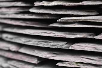 A close-up view of several stacked pieces of slate, showcasing their layered, rough textures and variations in thickness. The edges of each layer are visible, emphasizing the natural, irregular surface of the stone.