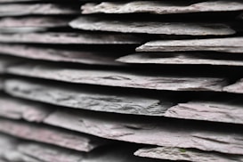 A close-up view of several stacked pieces of slate, showcasing their layered, rough textures and variations in thickness. The edges of each layer are visible, emphasizing the natural, irregular surface of the stone.