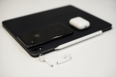 A collection of sleek electronic devices including a smartphone, tablet, stylus, wireless earbuds, and a charging case arranged on a white surface. The minimalist design and modern technology are accentuated by a monochrome color palette.