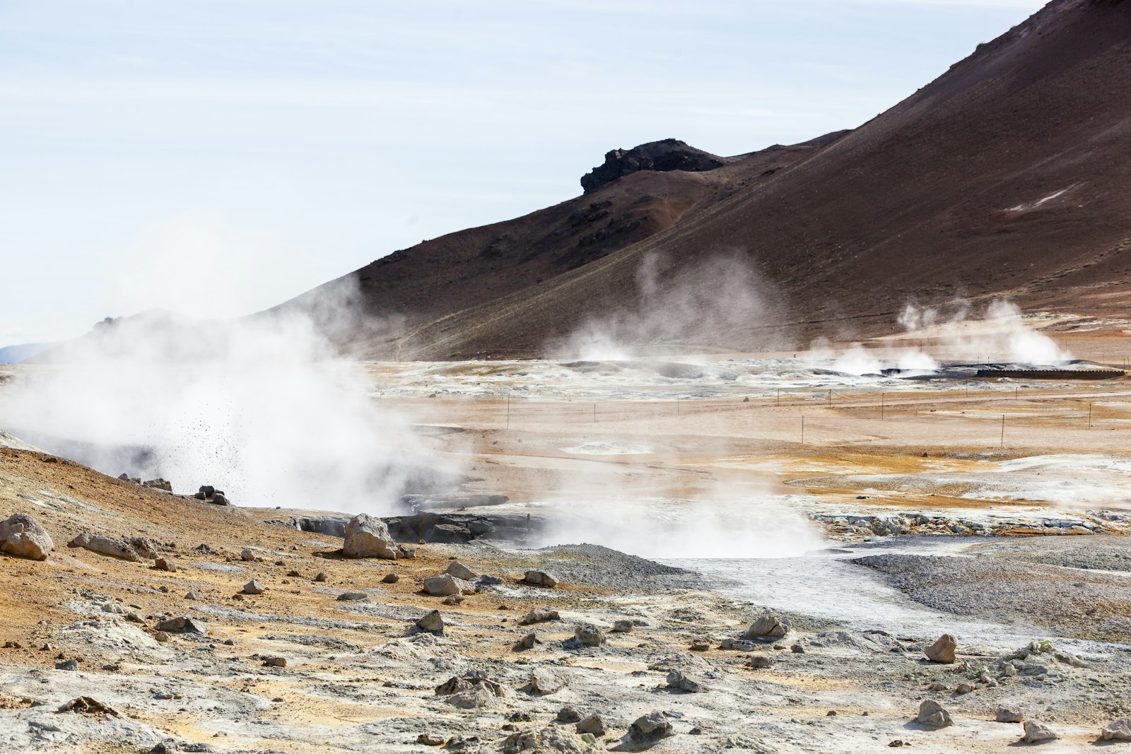 Steam rising from fumaroles across an ochre and gray geothermal field below the bare brown slope of Námafjall in north Iceland
