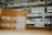 Shelves filled with neatly stacked cardboard boxes in a warehouse setting, with visible labels and numbers on each shelf. The focus is on organization and storage.