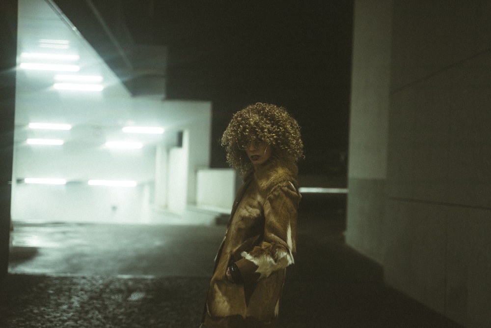 woman in brown coat standing near white wall