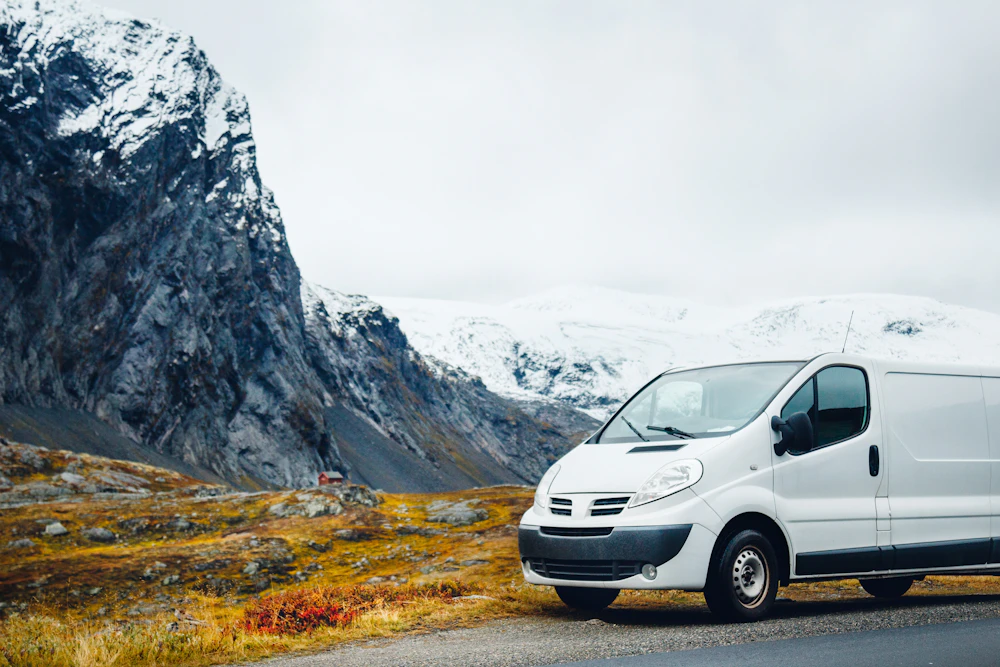 A white Northline service van parked on a mountain road below snow-covered peaks.