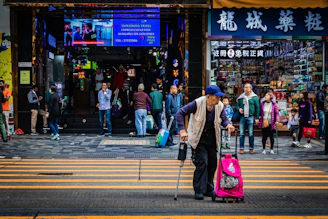 A cheerful helper assisting a senior crossing a small street in a lively neighborhood.