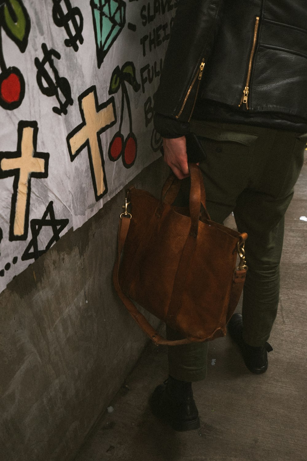 person wearing black leather jacket holding brown leather tote bag