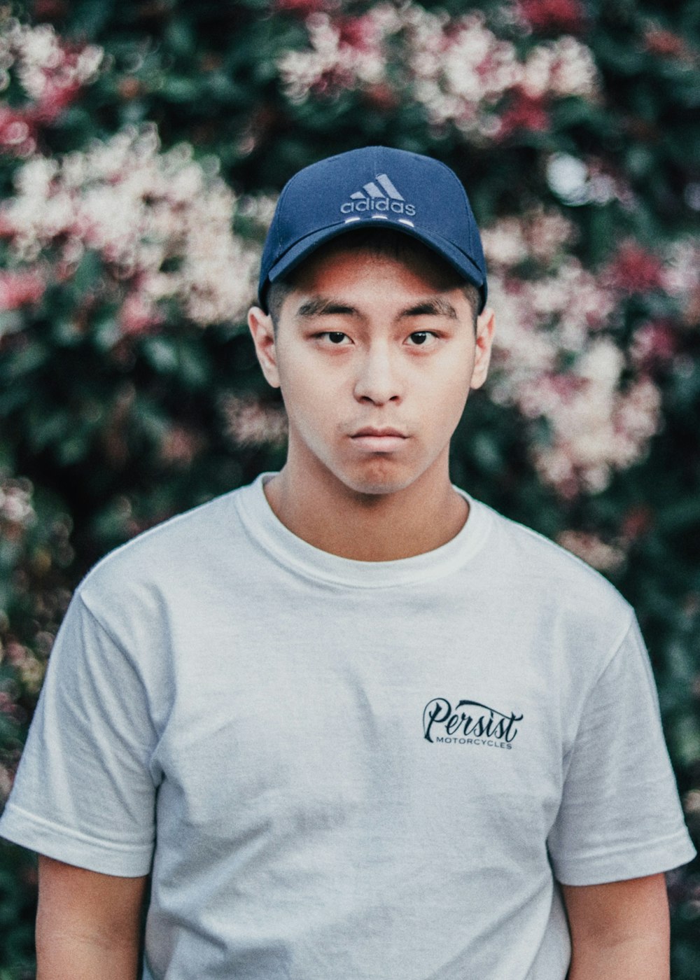 selective focus photography of man wearing blue adidas hat and white Persist crew-neck t-shirt